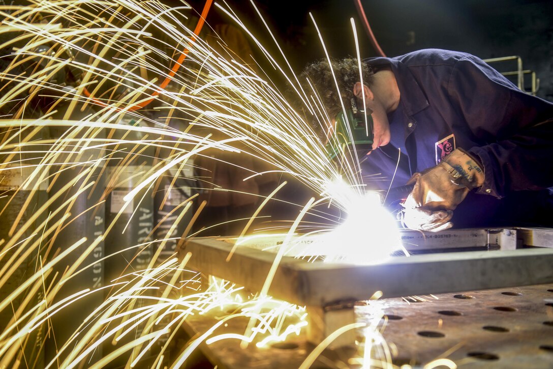 Sparks fly as a sailor wearing protective goggles cuts steel.