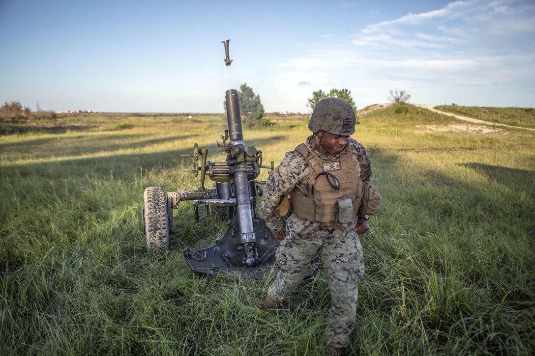 A Marine turns away and clenches his fists as a mortar system fires behind him.