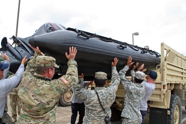 A group of guardsmen load a Zodiac boat on a vehicle.