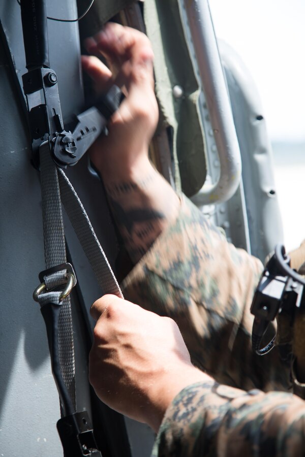 A U.S. Marine with the Maritime Raid Force, 26th Marine Expeditionary Unit (MEU), utilizes a ratchet strap to set up an aerial sniper position on a U.S. Navy MH-60S Seahawk helicopter with Helicopter Sea Combat Squadron 28 before conducting visit, board, search and seizure training during Realistic Urban Training (RUT) at Camp Davis Training Area - South, N.C., Aug. 20, 2017. RUT provides the MEU an opportunity to train in unfamiliar environments in preparation for an upcoming deployment at sea. (U.S. Marine Corps photo by Lance Cpl. Alexis C. Schneider)