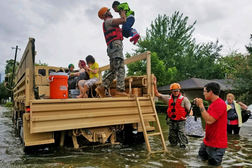 A soldier lifts a child onto a rescue vehicle in flood waters while others look on.