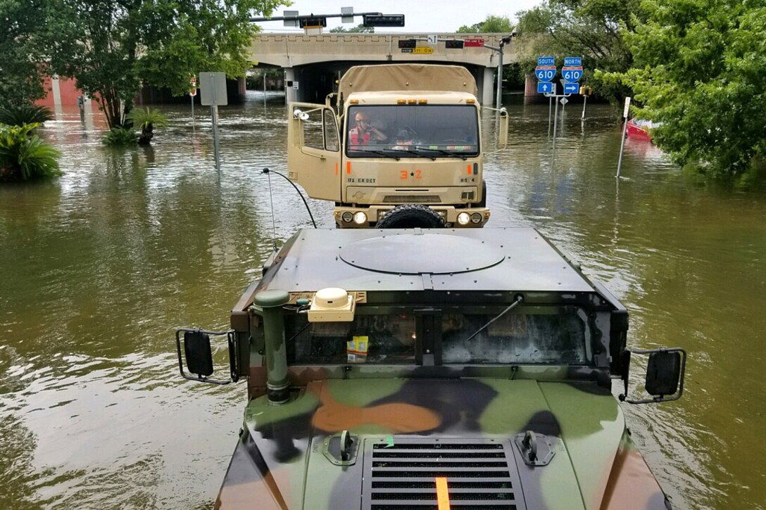 Texas National Guardsmen drive military vehicles down flooded streets while searching for stranded residents.
