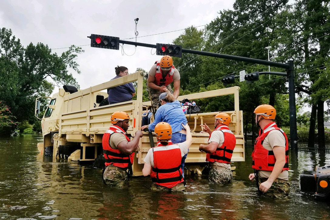 Texas National Guardsmen assist residents onto a military vehicle.