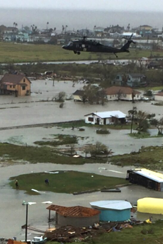 An Army UH-60 Black Hawk helicopter hovers over flooded buildings.