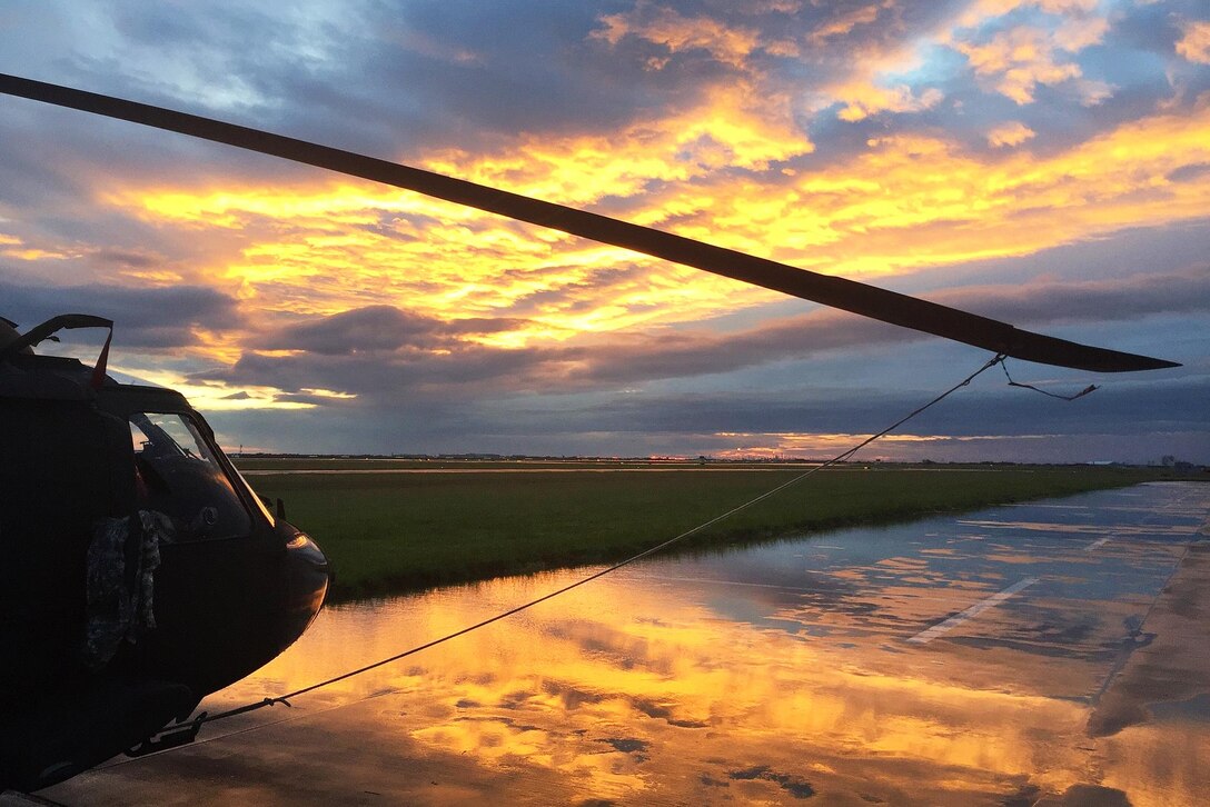 Texas National Guardsmen and Texas Task Force responders prepare a helicopter as the sun is reflected in the clouds.