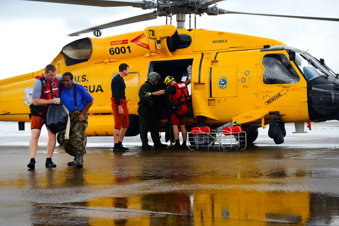Coast Guardsmen help off load displaced residents from a helicopter to a collection point.
