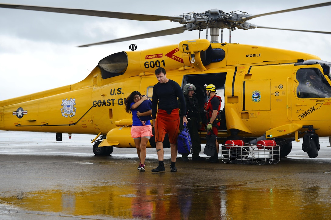A Coast Guardsman helps off load people from a  helicopter to a collection point.