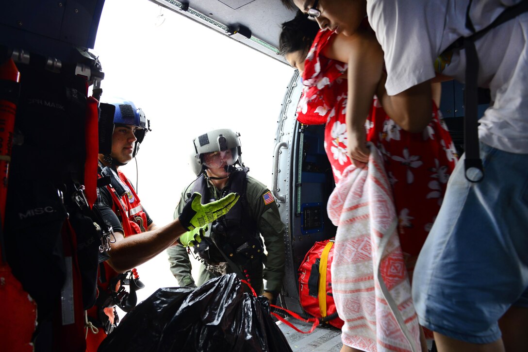 A member of the Coast Guard offers his hand to assist a woman and man out of a helicopter.