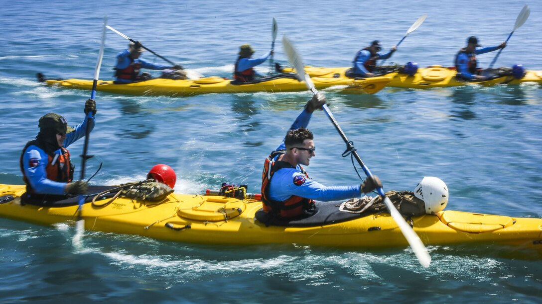 Service members in three kayaks paddle in the ocean.