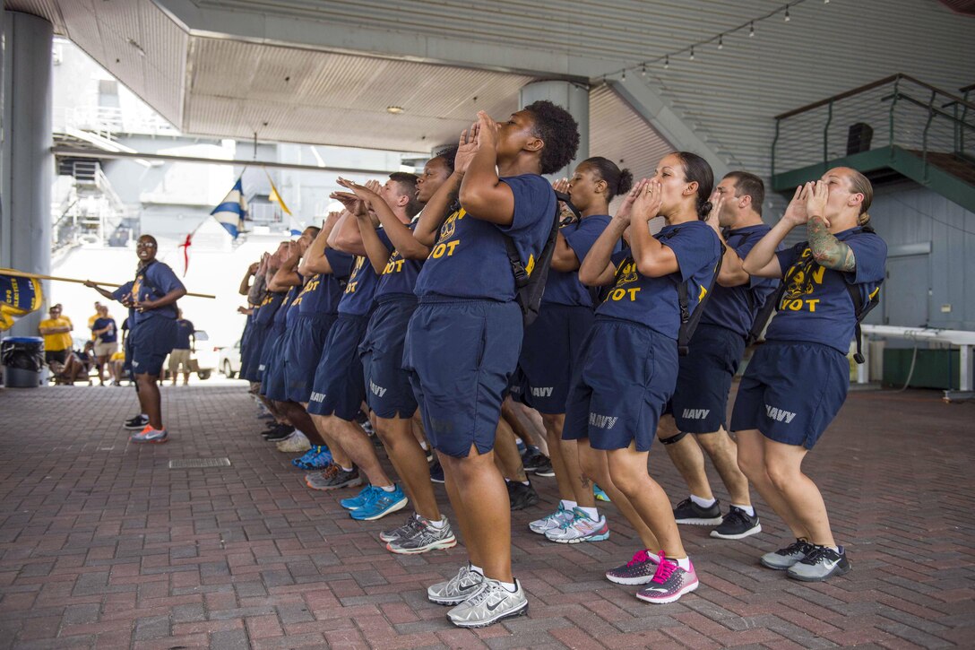 A group of sailors in formation hold their hands to their mouths as they call out a cadence.