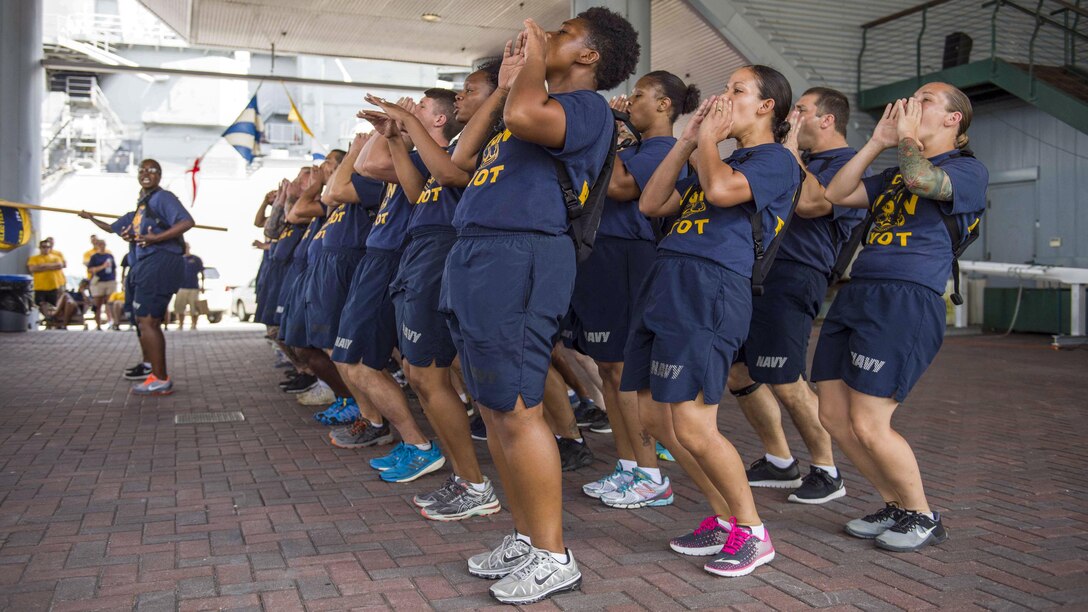 A group of sailors in formation hold their hands to their mouths as they call out a cadence.