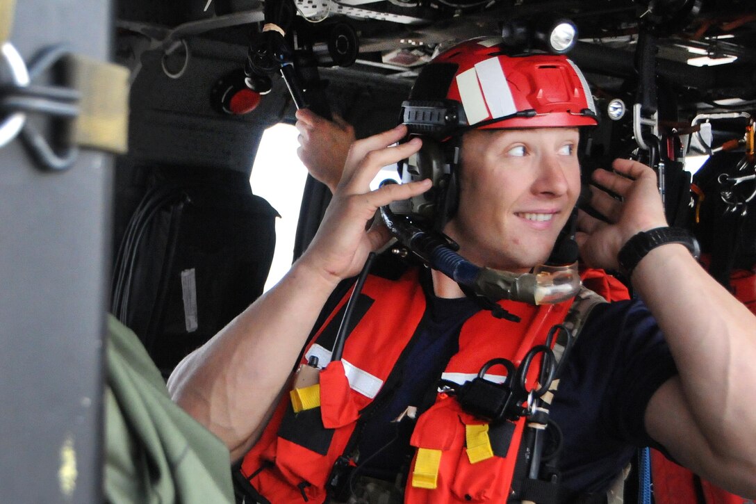 An airman adjusts his communication headset while sitting in a helicopter.