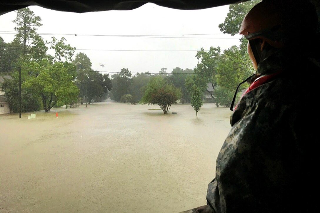 A guardsman drive looks out the back of a military vehicle at water and trees.