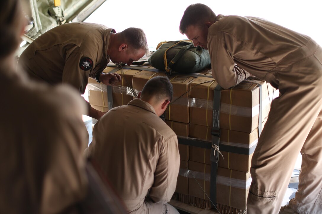 Two crew masters observe U.S. Marine Staff Sgt. Wesley Martins, a crew master with Marine Aerial Refueler Transport Squadron-352, Special Purpose Marine Air-Ground Task Force — Crisis Response — Central Command, tying  down a package onto a KC-130J Super Hercules in preparation for an air delivery exercise. Air delivery is a capability SPMAGTF CR-CC can employ that allows supplies to be delivered to ground troops when they are in remote locations, increasing SPMAGTF-CR-CC’s ability to support itself in austere expeditionary environments.