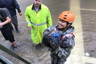 A guardsman holds a dog while standing in a flooded street.