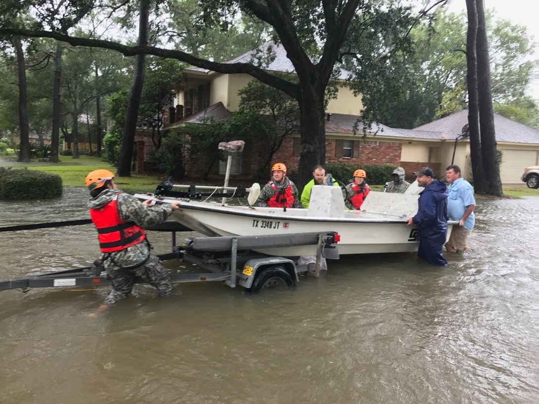Guardsmen and civilians push a boat onto a trailer during search and rescue mission.