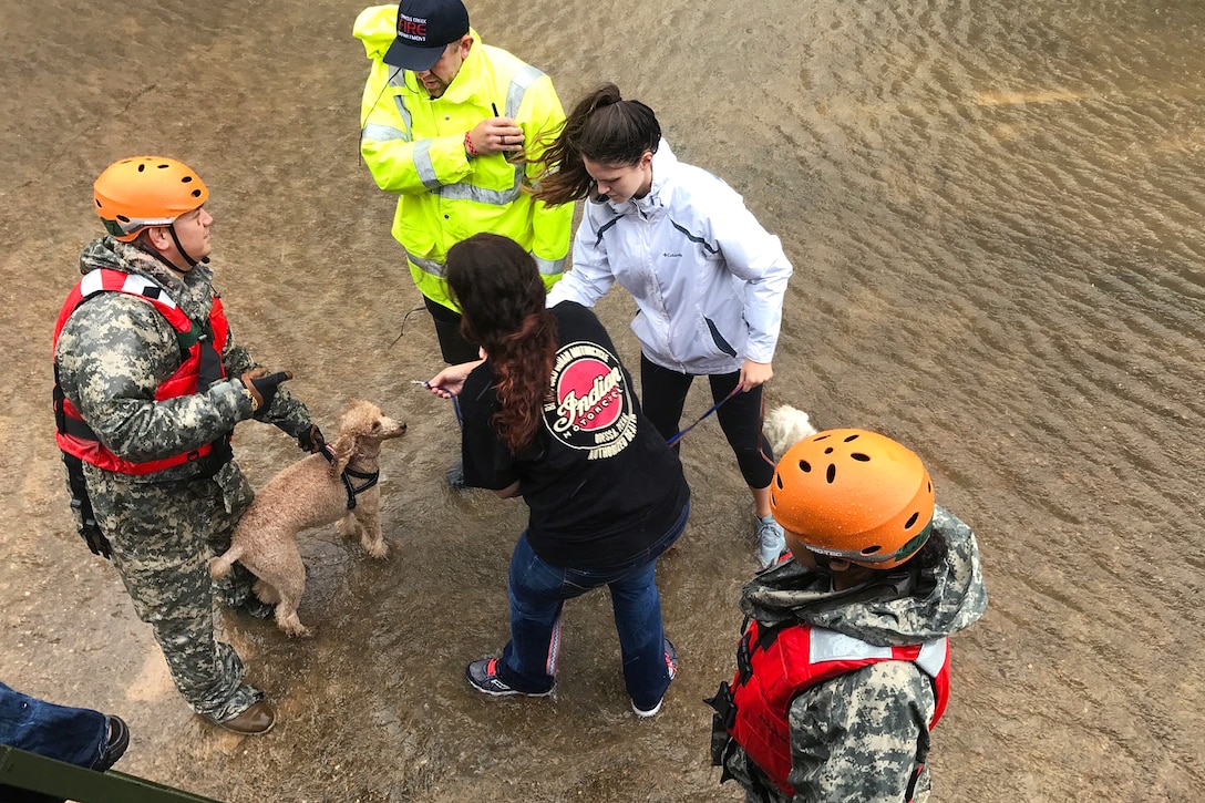 A guardsmen and a first responder help displaced residents and their pet loading them into a military vehicle.