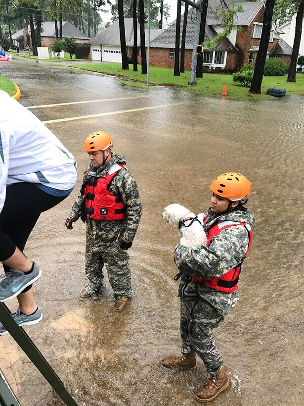 Guardsmen help displaced residents and a pet into a military vehicle.