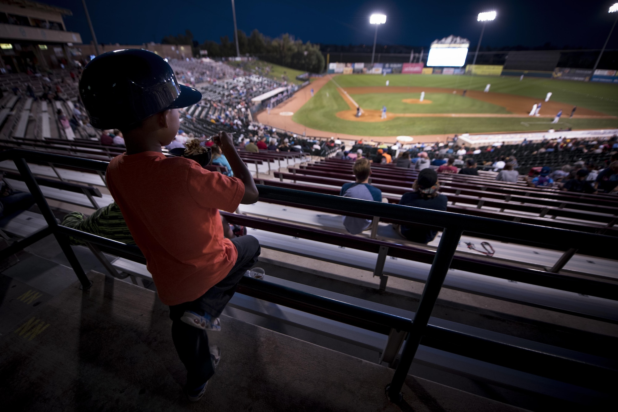 A boy attending a Snowflake Event at Security Service Field watches a Sky Sox baseball game while eating ice cream in Colorado Springs, Colo., Aug. 21, 2017. A Snowflake event is a regional occurrence hosted for Snowball Express families. Since 2006, Snowball Express has provided hope and happy memories to the children of military fallen heroes who have died while on active duty since 9/11. (U.S. Air Force photo by Senior Airman Dennis Hoffman)