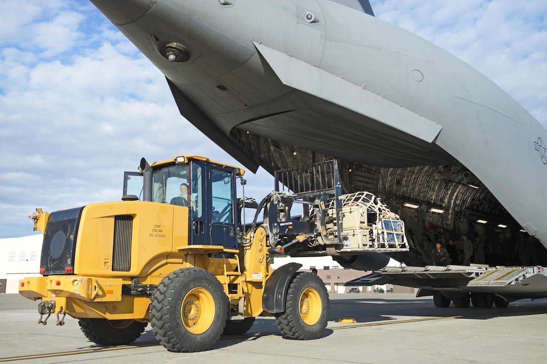 An airman uses a heavy forklift to load cargo and equipment onto a plane.