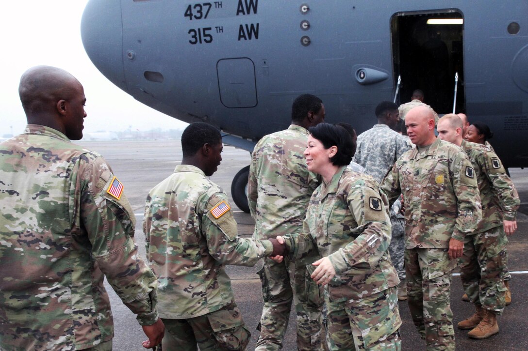 Soldiers shake the commander's hand as they get on an airplane.