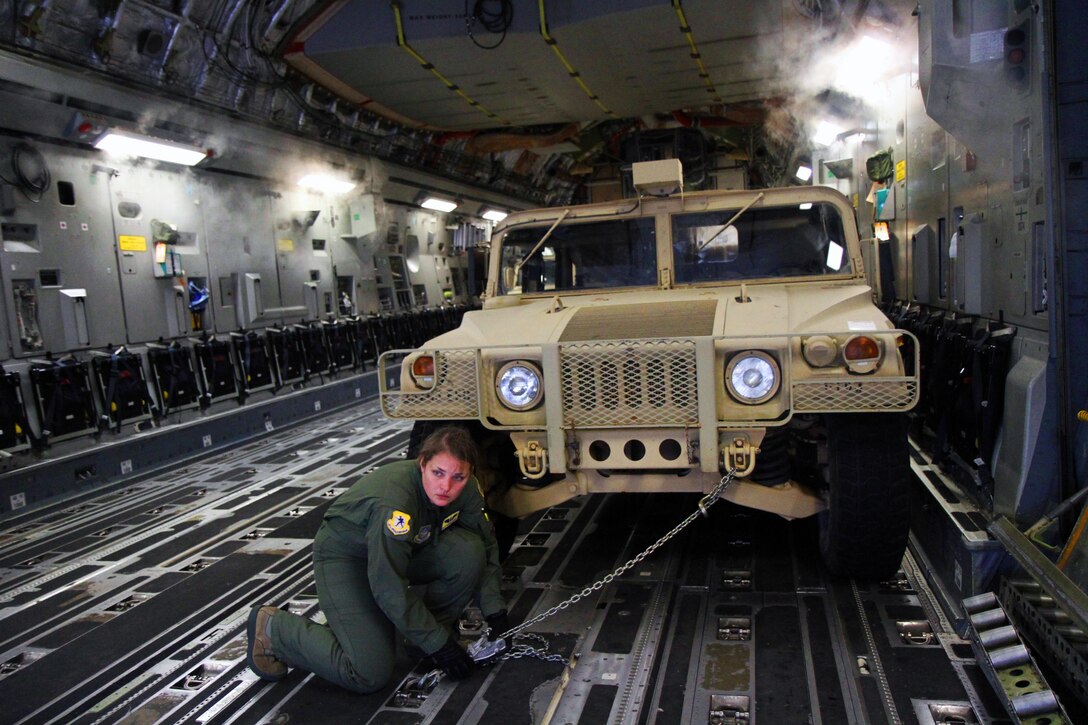 An airman ties a military vehicle to a plane's cargo hold.