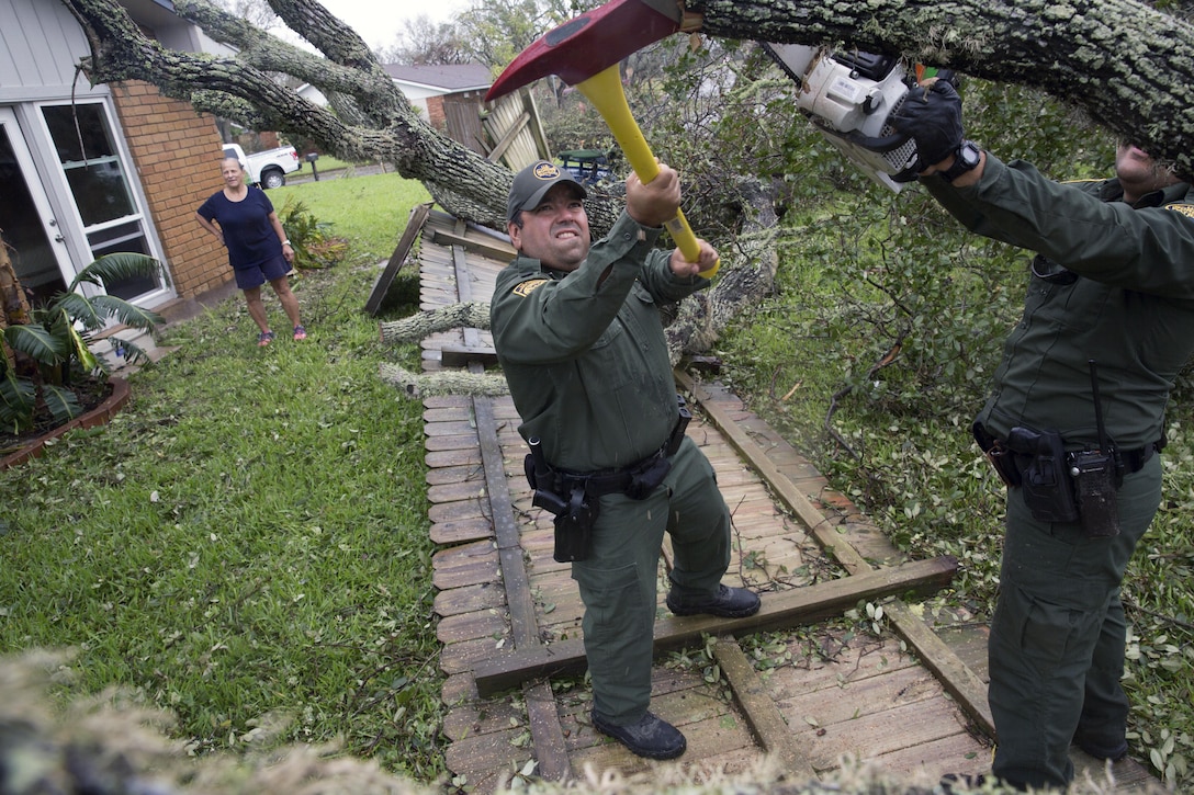 Two boarder patrol agents cut trees using an ax and a chainsaw.