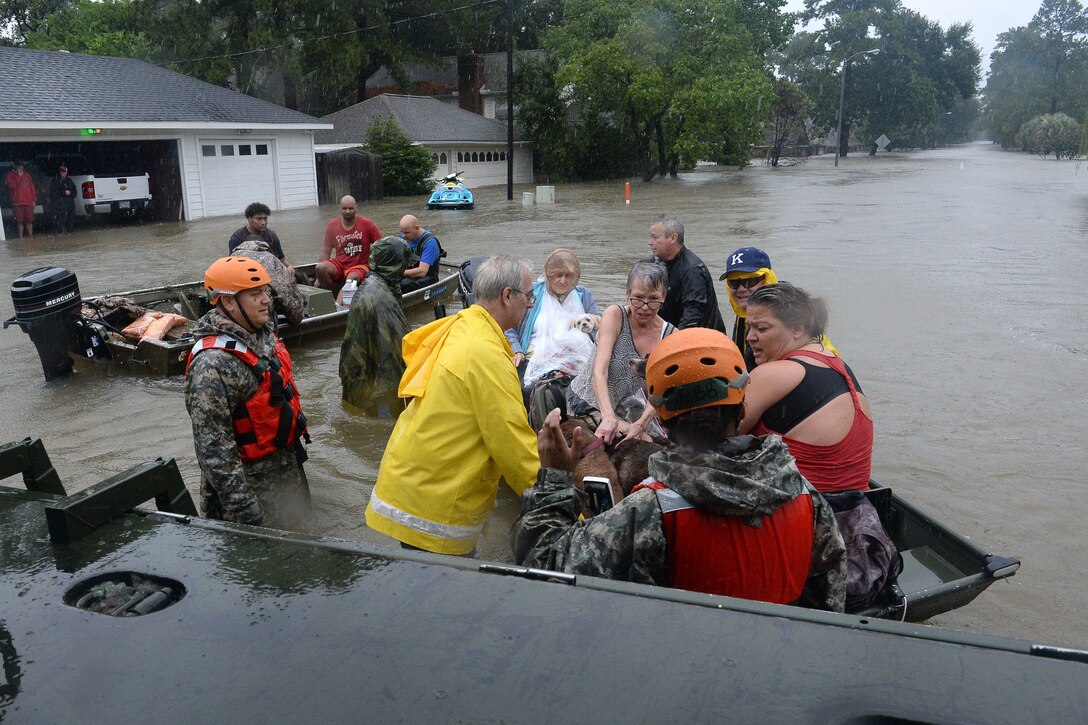 A group of guardsmen and first responders help people into a boat in floodwaters.
