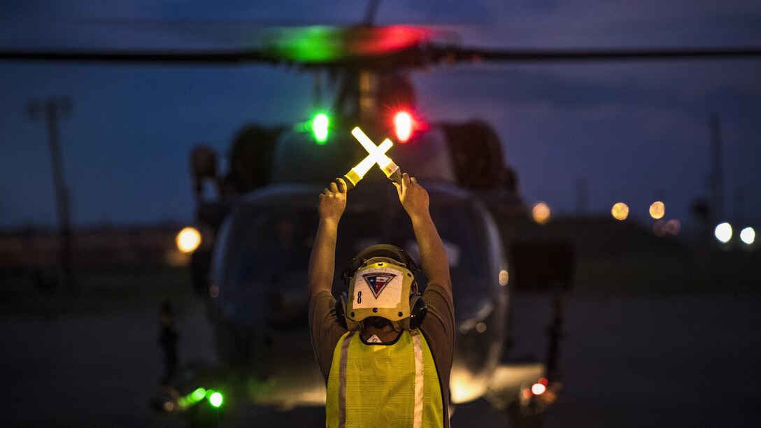 A sailor signals a helicopter on the ground at night.