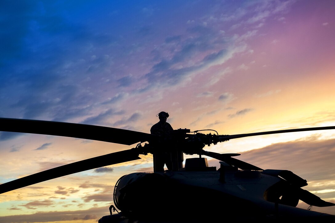 An airman stands on a helicopter to check the rotor blades.