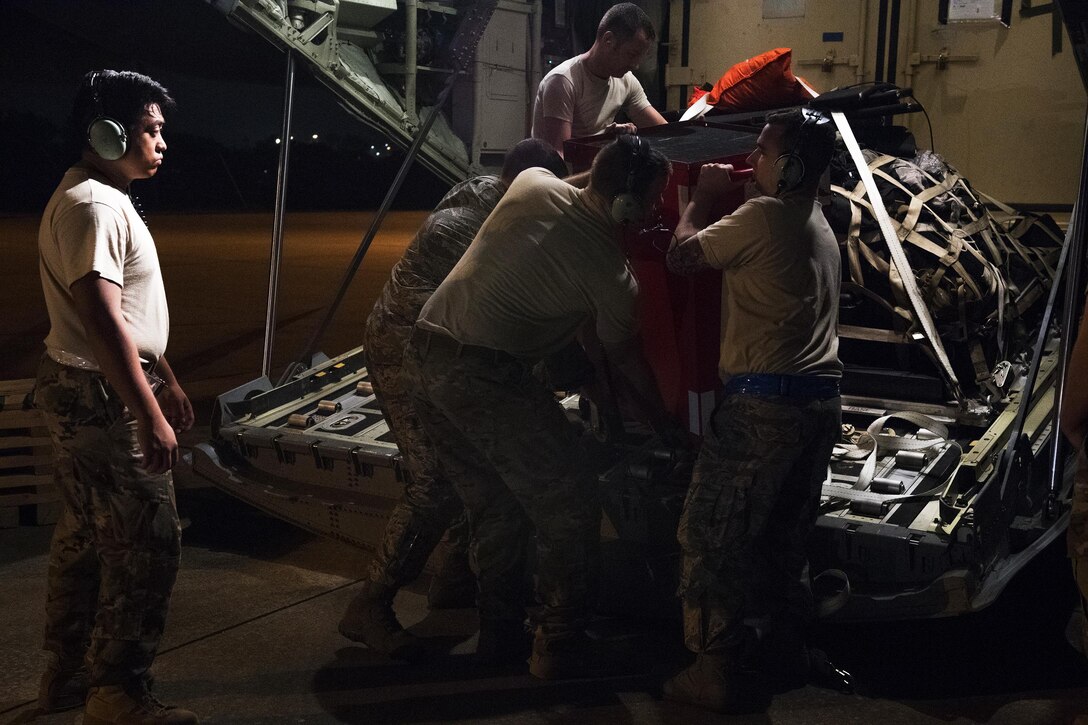 A group of airmen unload cargo from the back of an airplane.