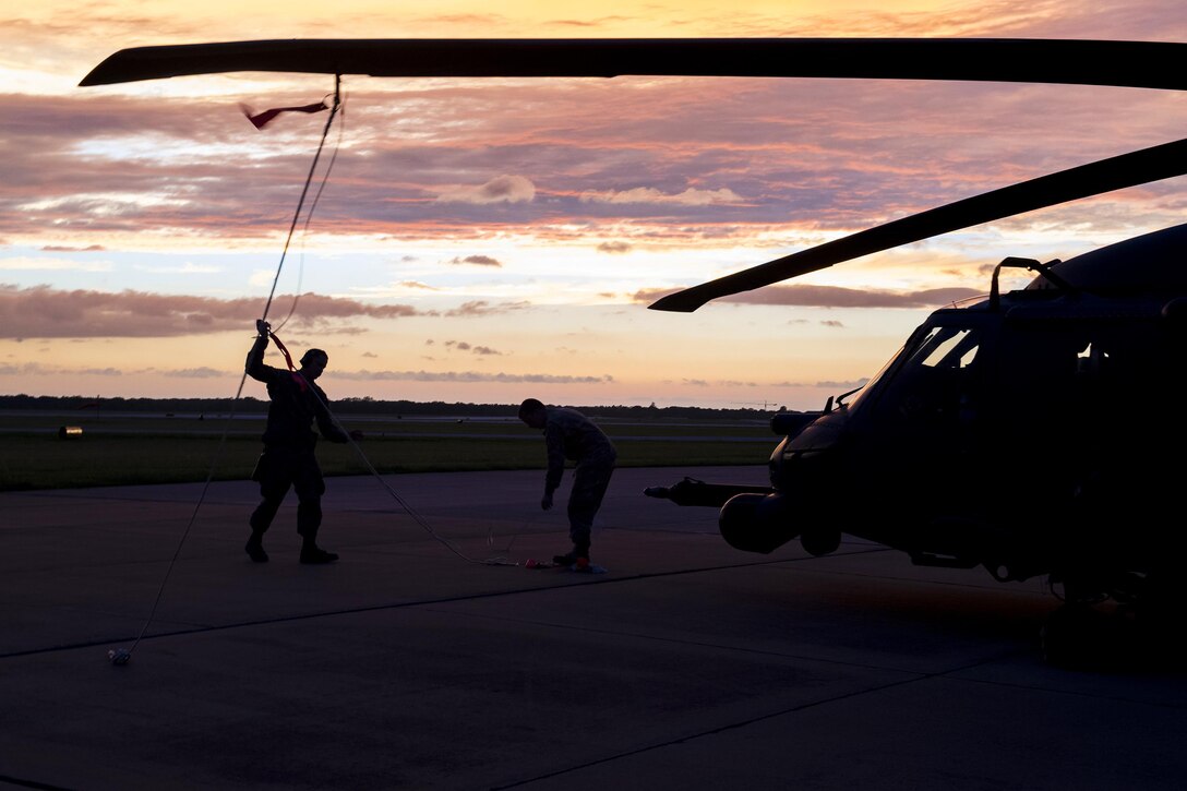 Airmen have a rope tied to a helicopter rotor blade.