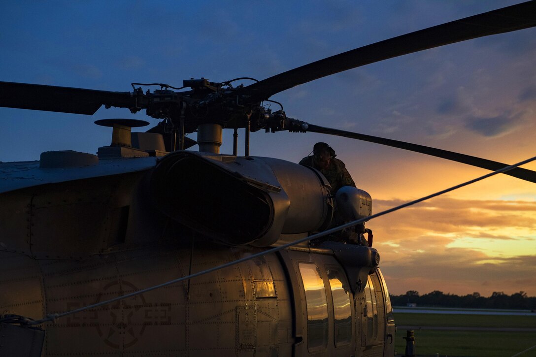 An airman is on top of a helicopter inspecting the rotor blades.