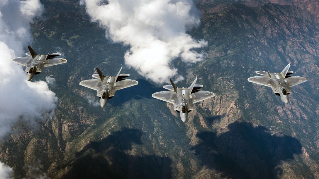 Four fighter jets fly over a mountain range.