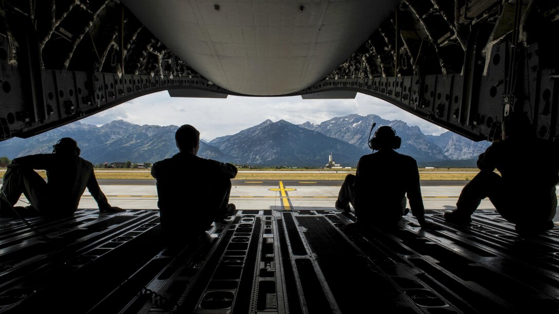 Four airmen sit in an aircraft and look at the Teton Range.