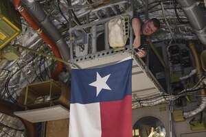 Senior Airman Justin Hampton, 16th Airlift Squadron loadmaster, hangs the state flag of Texas prior to takeoff of a disaster relief mission Aug. 29.