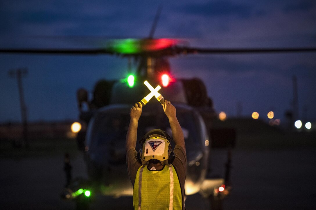 A sailor signals a helicopter on the ground at night.