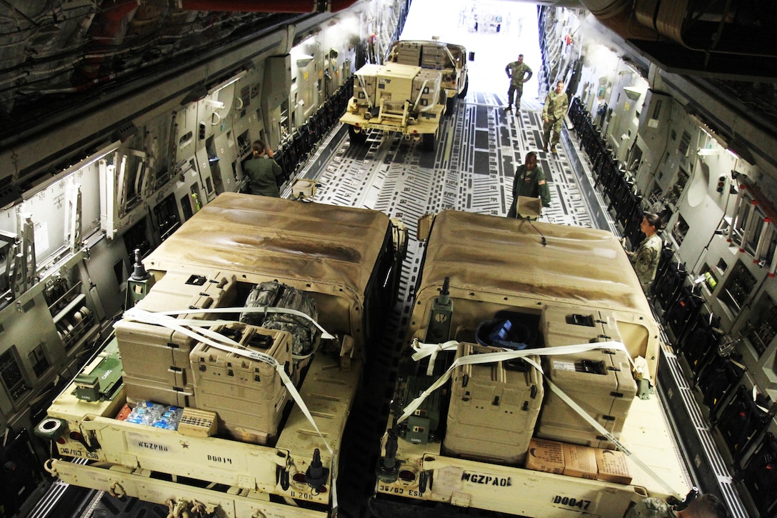 Soldiers sand with military vehicles inside an airplane.