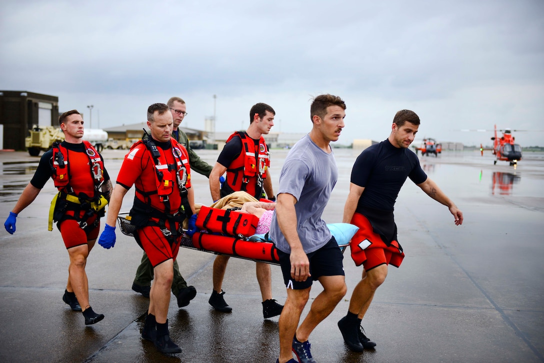 Members of the Coast Guard carry a displaced resident to a MH-65 Dolphin helicopter