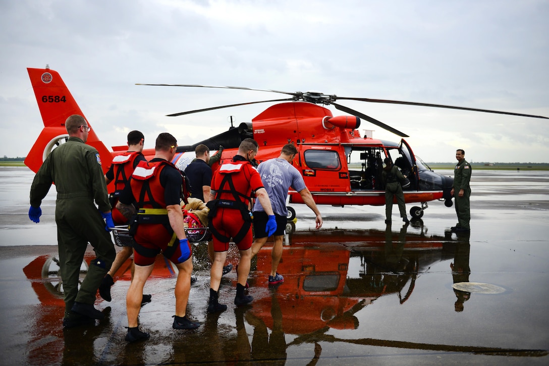 Members of the Coast Guard carry a displaced resident to a MH-65 Dolphin helicopter