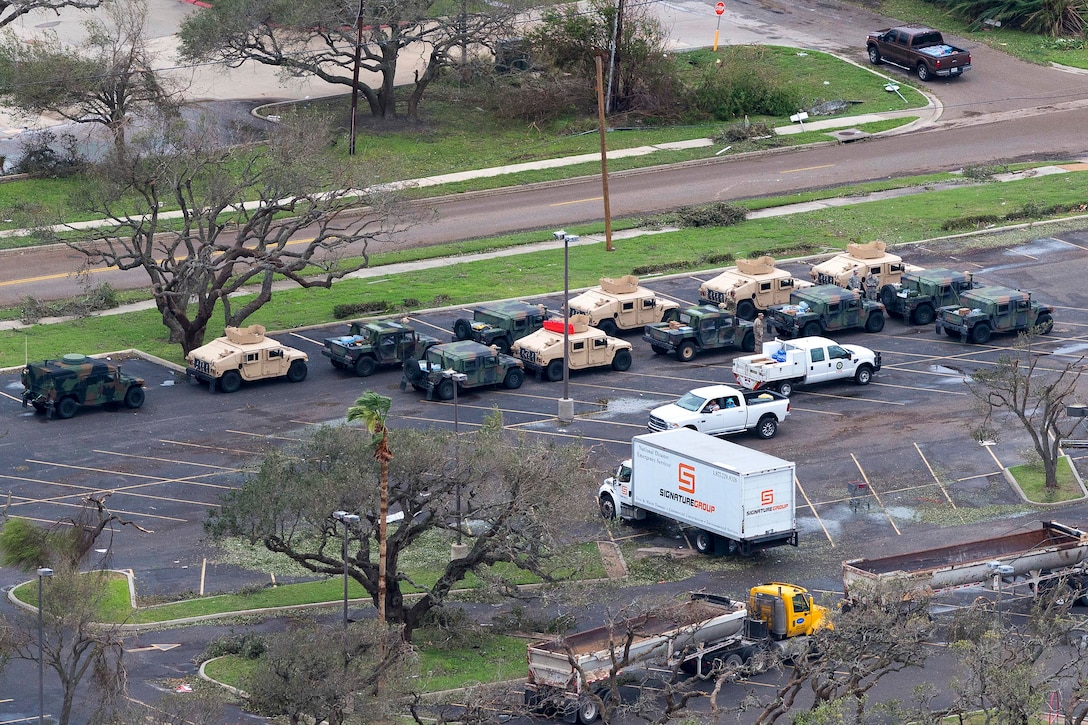 An aerial view shows National Guard vehicles assembled in a parking lot to setting up a collection point for displaced residents.