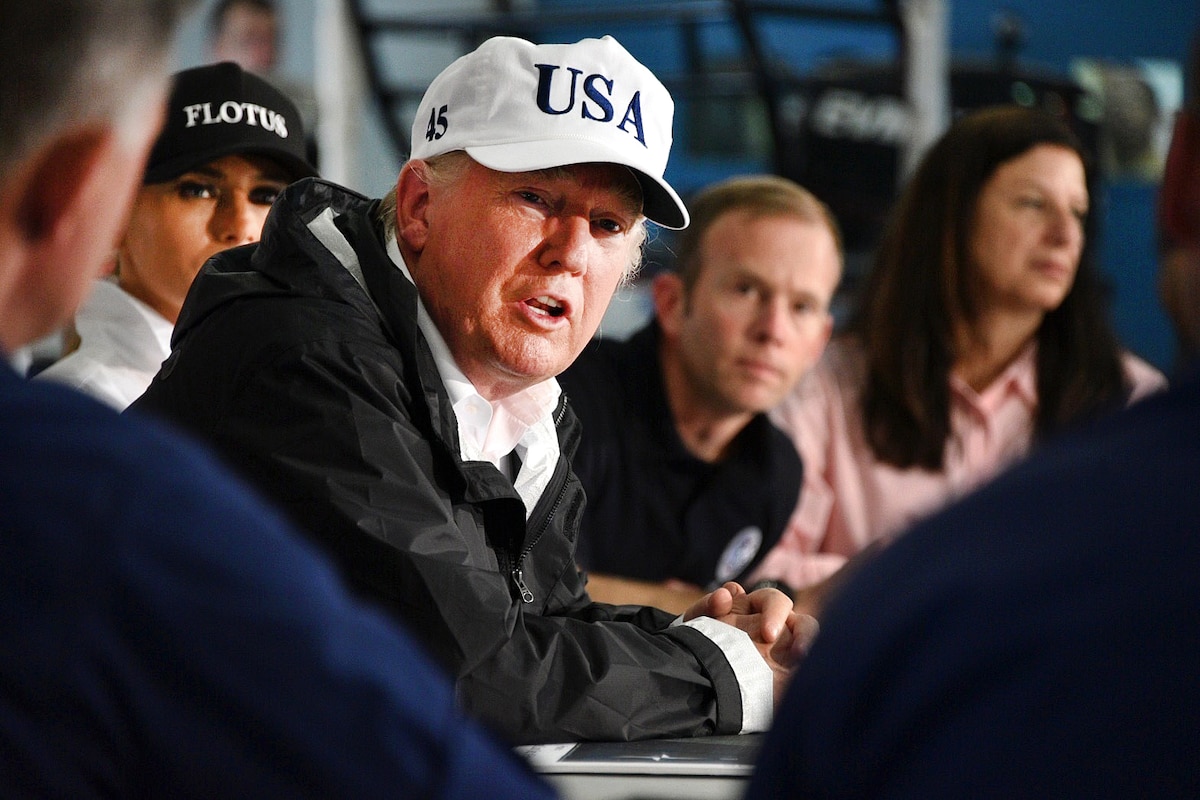 President Donald Trump speaks to people at a table during a briefing.