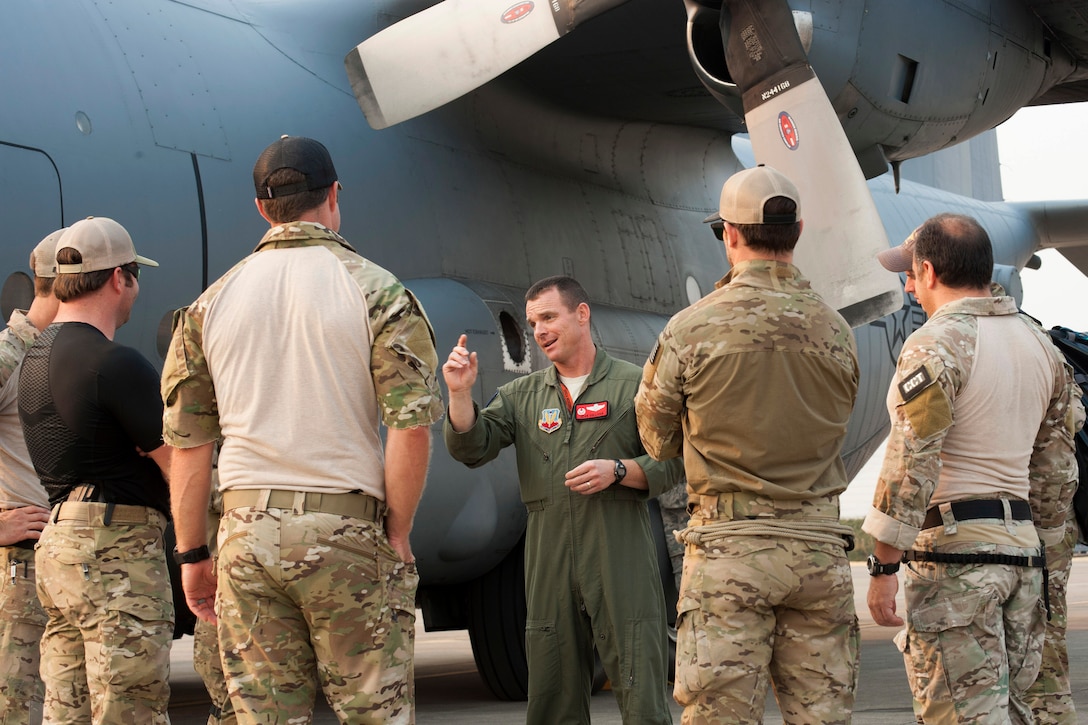 An airman briefs fellow troops gathered by an aircraft on a flight line.
