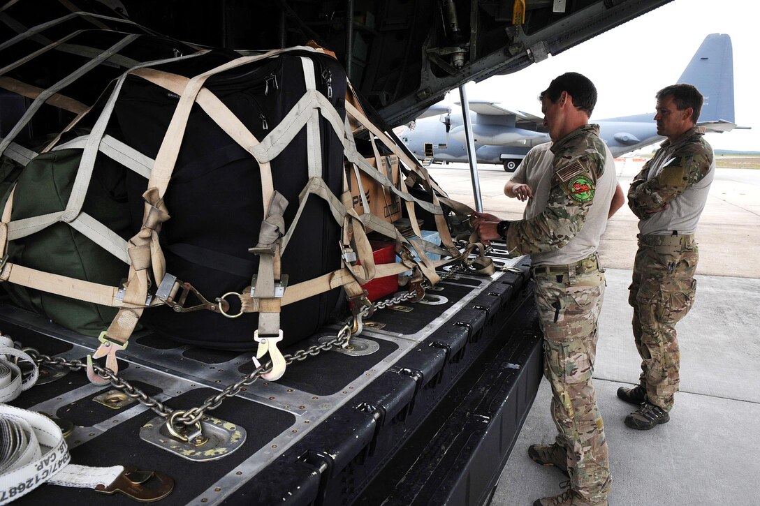 Airmen tighten down cargo straps, securing supplies onto a HC-130 Hercules aircraft.