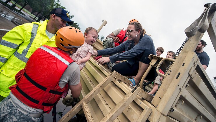 A soldier lifts a crying child into the arms of a woman during a rescue operation.