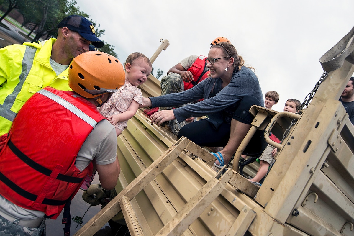 A soldier lifts a crying child into the arms of a woman during a rescue operation