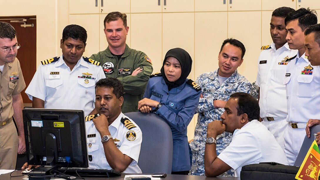Sailors from several countries look at a computer screen.