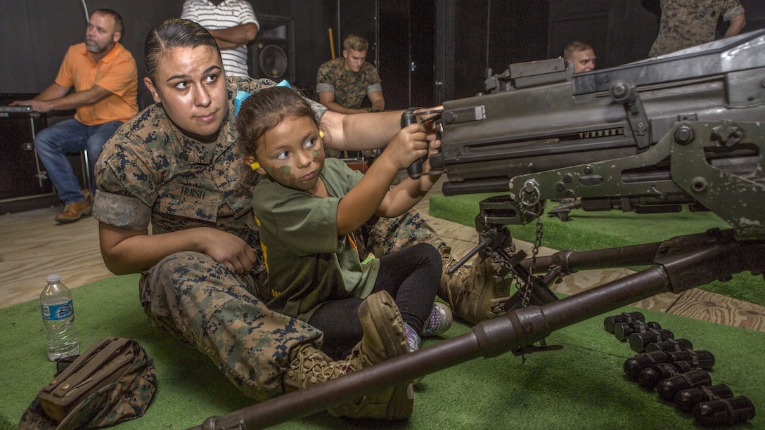 A Marine and child practice operating a simulated machine weapon.