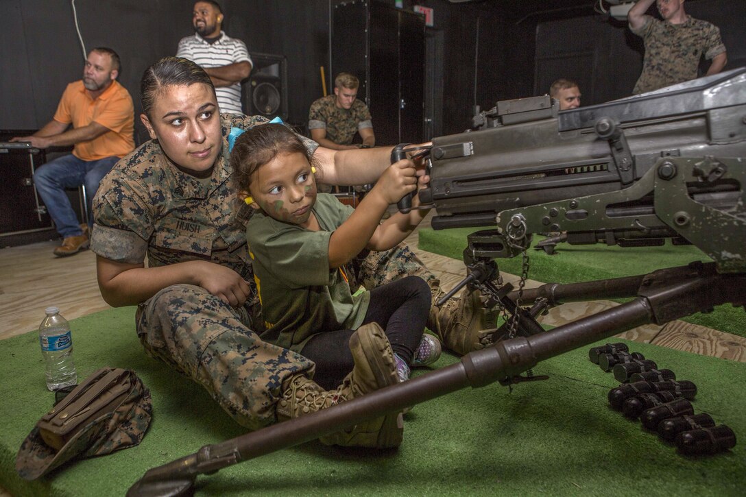 A Marine and child practice operating a simulated machine weapon.