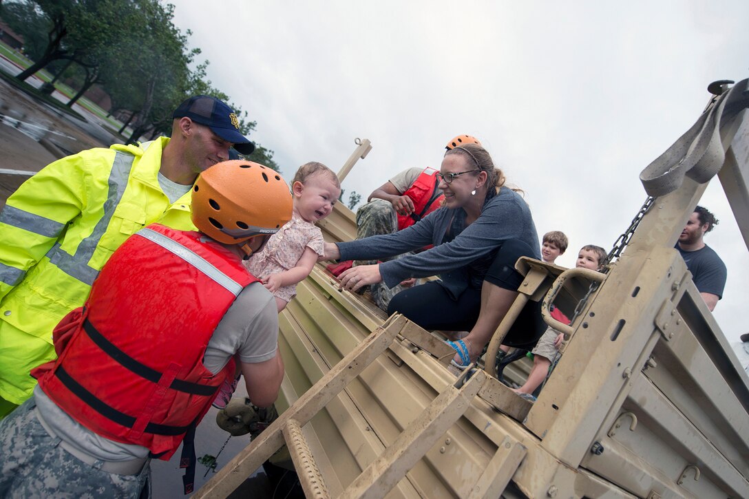 A soldier lifts a child into a vehicle during rescue operations.